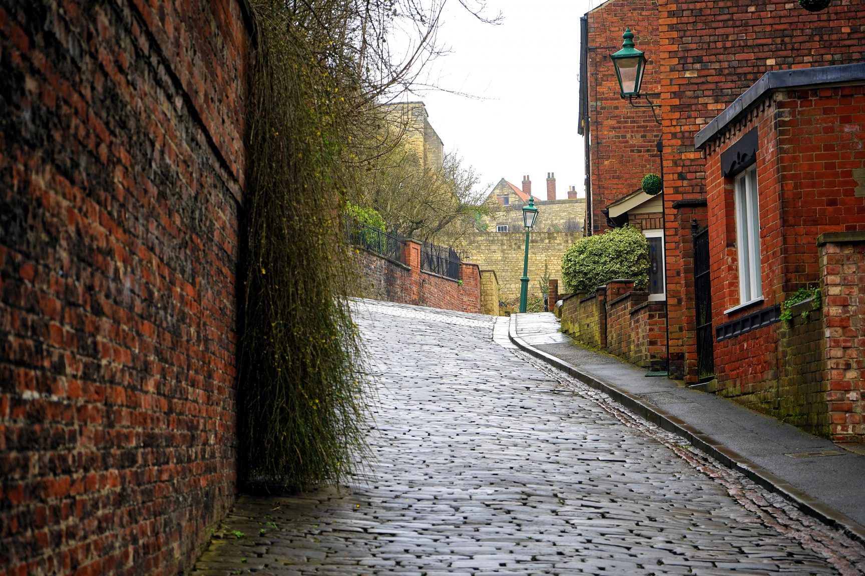 A small cobbled street, with red brick houses. It's a grey day and the street is damp.