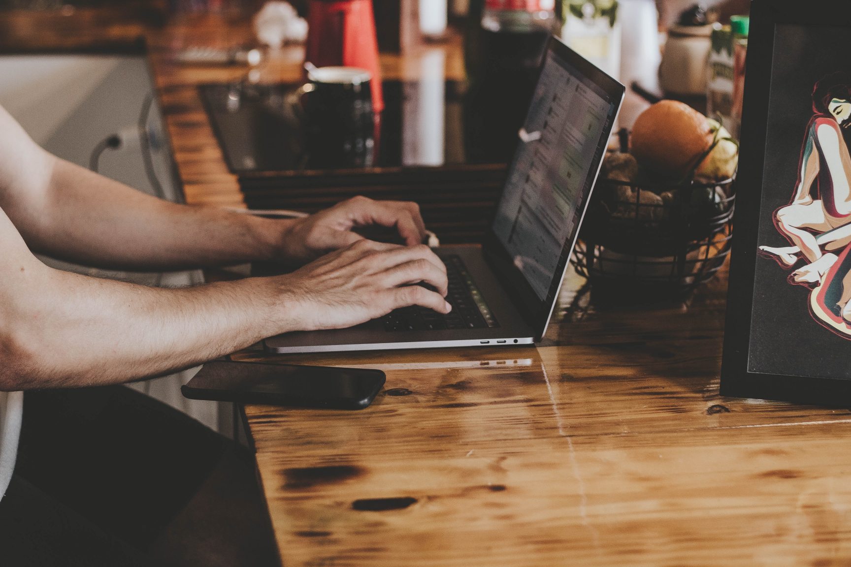 Someone at a laptop working. The table is wooden and shiny.