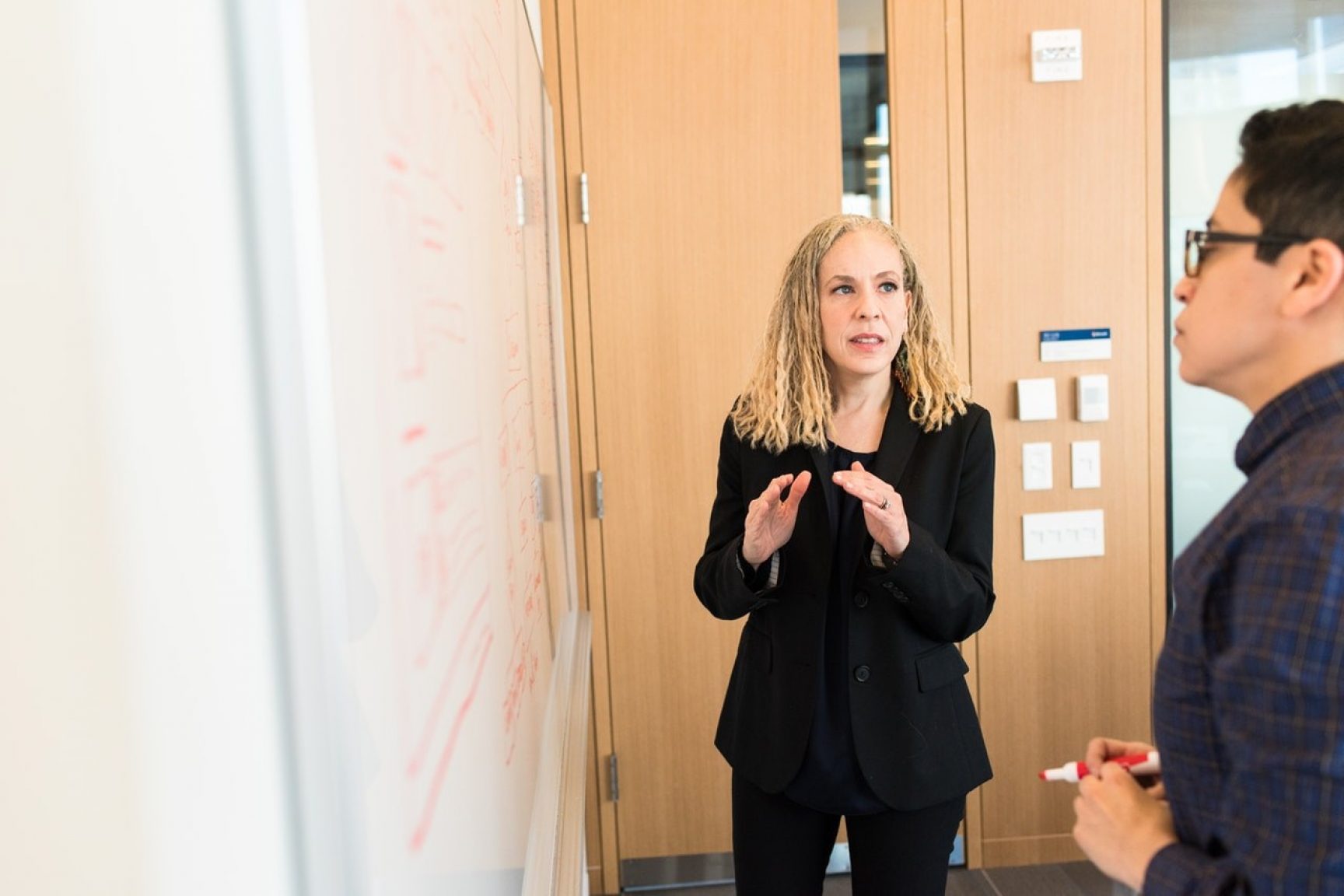 A woman and a man having a conversation in a meeting room. They are discussing something on a whiteboard.