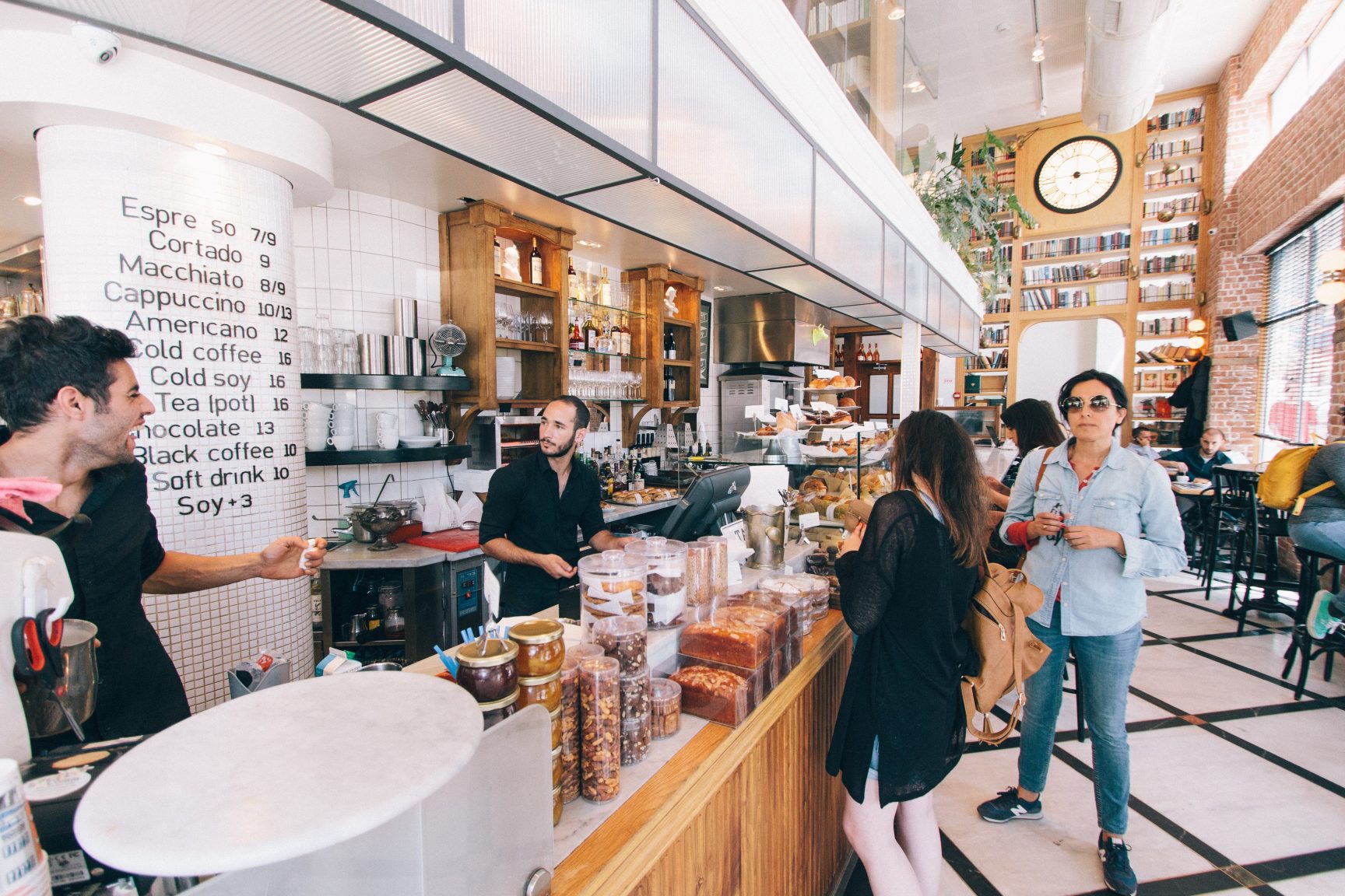 A nice bright airy coffee shop, there are two people serving behind the counter. There are a few people queuing.